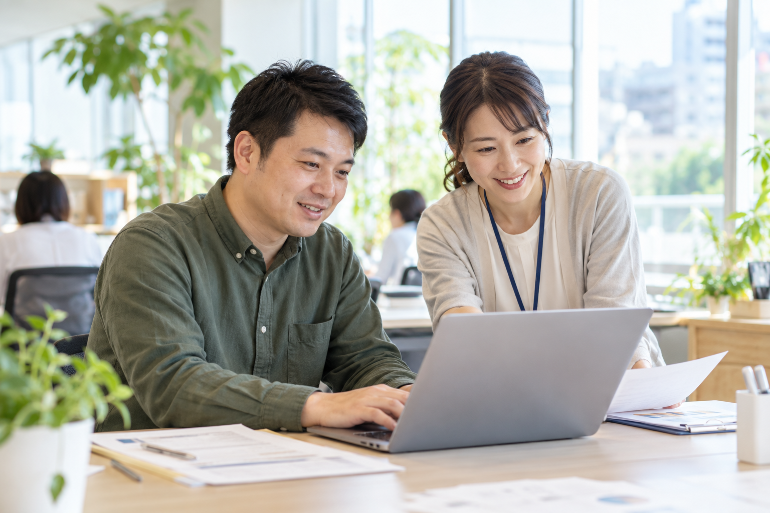 明るいオフィスでパソコン業務の相談をする様子（AI生成イメージ）